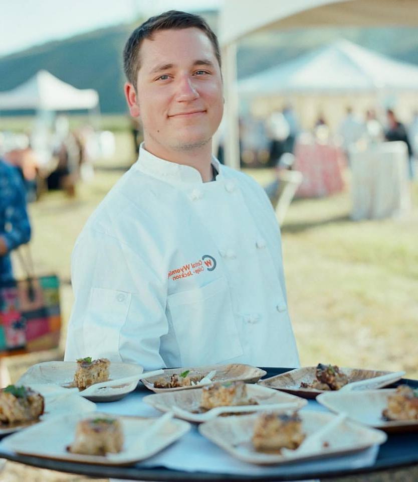 Zack Ward culinary student in smock in front of dessert table